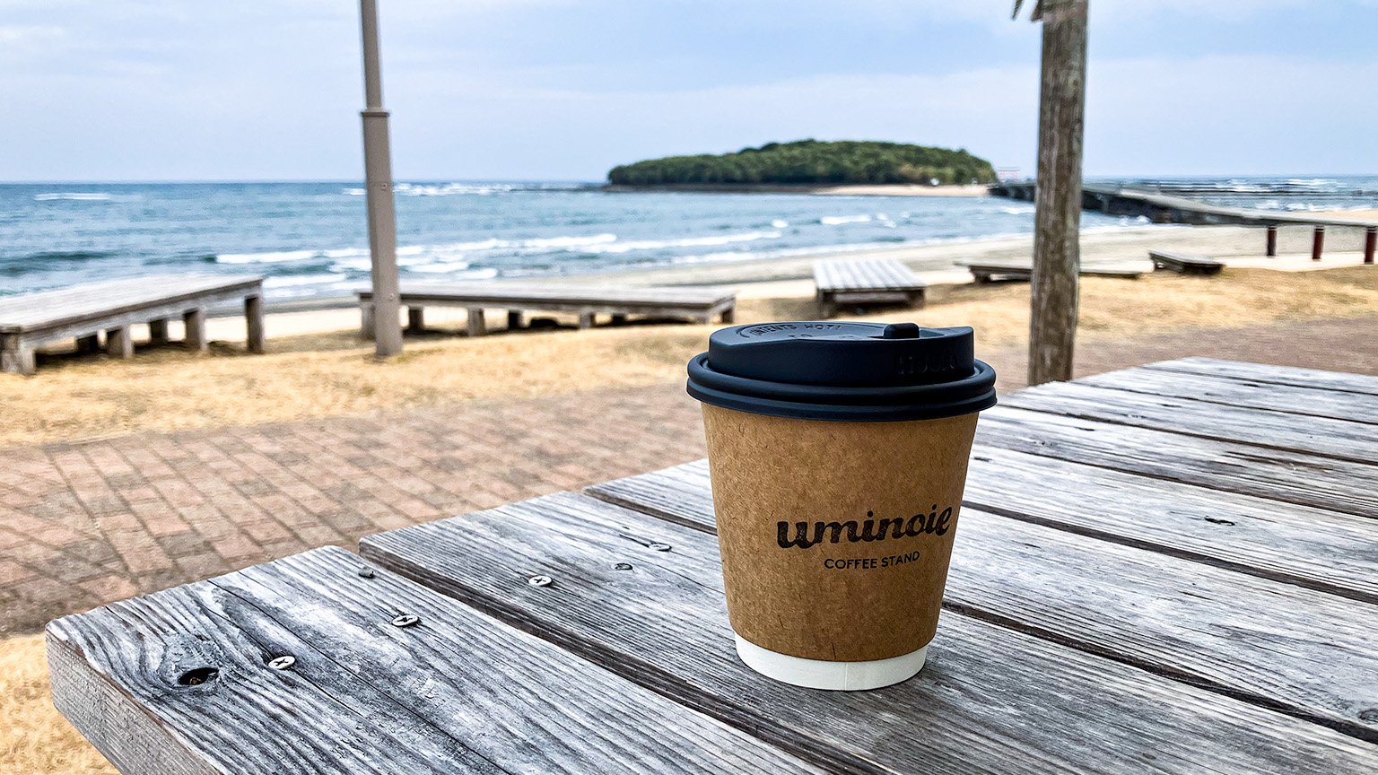 青島ビーチパーク内の uminoie coffee stand のカフェラテと青島の写真